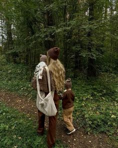 a woman and child are walking through the woods with backpacks on their back,