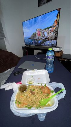 a table with a tray of food and a bottle of water on it next to a flat screen tv