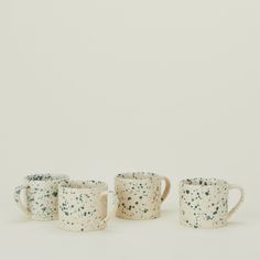 four mugs with speckles on them are lined up against a white background