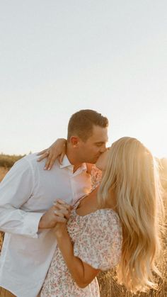 a man and woman kissing in the middle of an open field with tall grass behind them