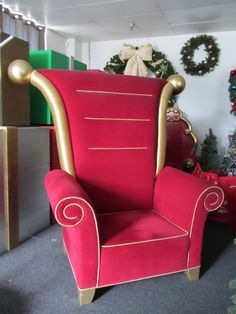 a red chair with gold arms in front of christmas trees and presents on the floor