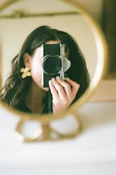 a woman holding a camera in front of a mirror