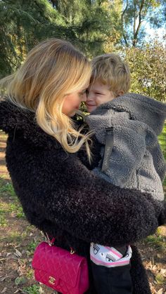 a woman holding a child in her arms and wearing a black coat with fur on it