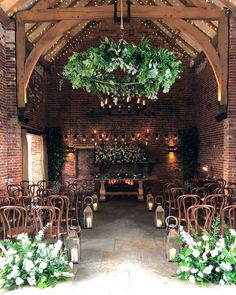 an indoor wedding venue set up with wooden chairs and greenery hanging from the ceiling