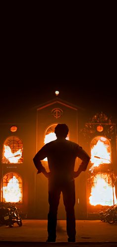 a man standing in front of a large building with fire coming out of it's windows