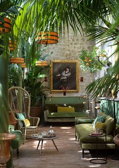 a living room filled with lots of green furniture and potted plants on the wall