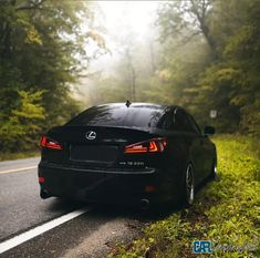 a black car is parked on the side of the road in front of some trees