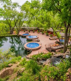 an outdoor swimming pool surrounded by lush green trees and water features two hot tubs