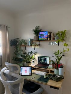 a desk with a computer, laptop and plants on it in a home office area