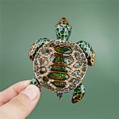 a hand holding a turtle brooch with green and gold decorations on it's shell