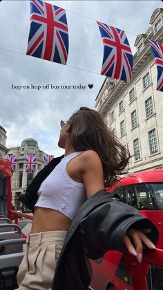 a woman standing next to a red car with british flags flying in the air above her