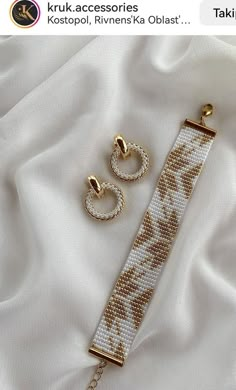 two pieces of jewelry sitting on top of a white cloth covered bedding with gold chains