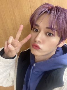 a person with purple hair making the peace sign