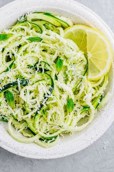 a white bowl filled with zucchini noodles and topped with lemon wedges next to a fork