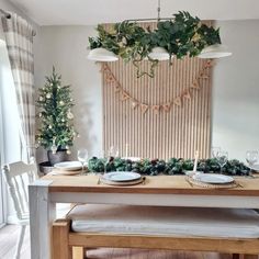 a dining room table with place settings and greenery on the wall hanging over it