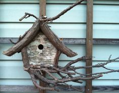 a birdhouse made out of branches on the side of a building with a blue wall behind it