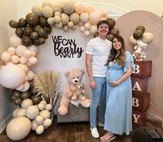 a pregnant couple standing in front of a backdrop made out of balloons and teddy bears