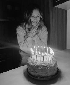 a woman sitting in front of a cake with lit candles