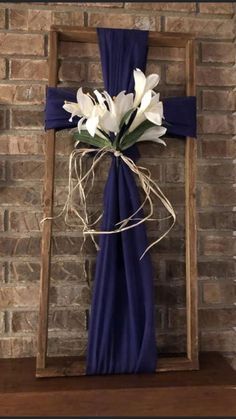 a wooden cross with flowers in it sitting on a shelf next to a brick wall