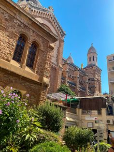 an old building in the middle of a garden with purple flowers and greenery around it