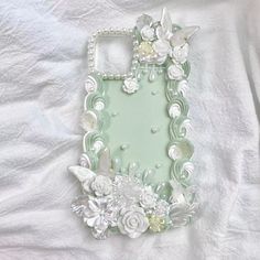 a cell phone case with flowers and pearls on the front, sitting on a white sheet