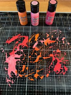 three bottles of paint sitting on top of a table next to a cutting board with some type of artwork