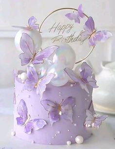 a birthday cake with purple butterflies and pearls on the top is decorated with a happy birthday sign