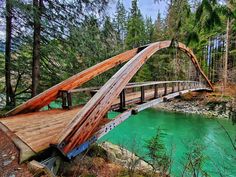 a wooden bridge over a green river surrounded by trees in the woods with water running under it