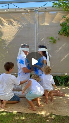 a group of people sitting on top of a mat in front of a white tent