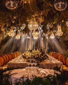 a table is set with candles, wine glasses and flowers in front of the chandelier