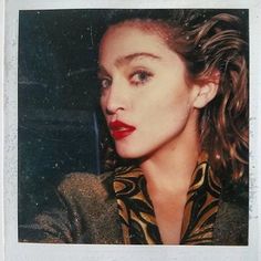 a close up of a person wearing a jacket and red lipstick on her face with long curly hair