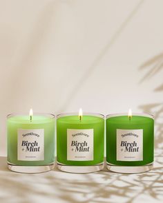 three green candles sitting next to each other in front of a white wall with the words birch and mint on it