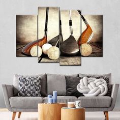 three golf clubs and two balls on a table in front of a gray couch with white pillows