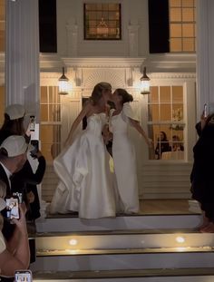 two women in white dresses are walking down the stairs with cameras around them and people taking pictures