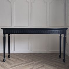 a black bench sitting on top of a hard wood floor next to white paneled walls