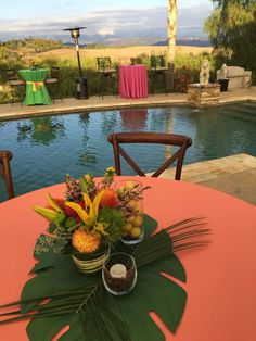 a table with flowers and fruit on it next to a pool