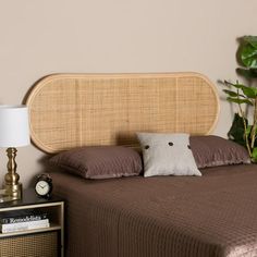 a bed with brown sheets and pillows next to a night stand, lamp and potted plant