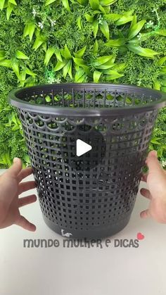 a person holding a black plastic basket in front of a green wall