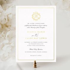 a white and gold wedding card with the letter b on it, surrounded by flowers