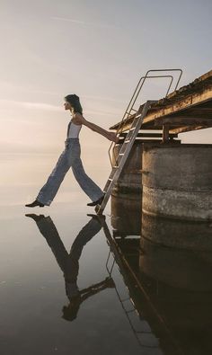 a woman is walking on the water with her hand in her pocket and she is wearing overalls