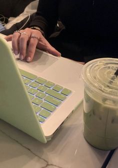 a woman sitting at a table using a laptop computer with a drink in front of her