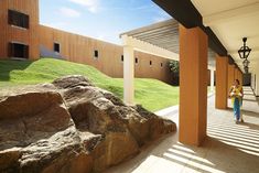 a woman walking down a walkway next to a large rock formation on the side of a building