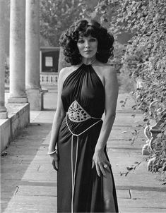 an old photo of a woman in a long black dress standing on the sidewalk with her hand on her hip