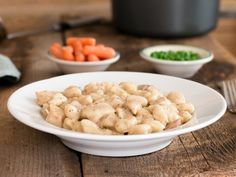 a white bowl filled with food next to bowls of carrots, peas and broccoli