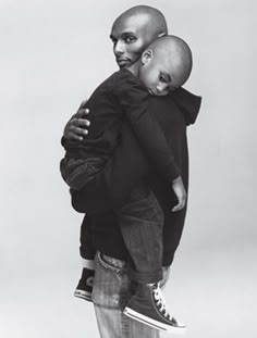 a black and white photo of a man holding a young child in his arms while standing on top of a skateboard