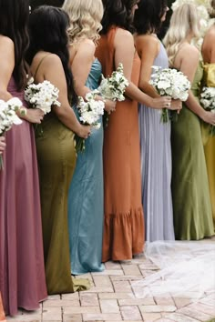 a group of women standing next to each other wearing dresses and holding bouquets in their hands