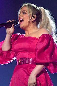 a woman in a pink dress singing into a microphone