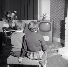 two children sitting on a chair watching tv