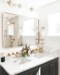 a bathroom with marble counter tops and gold accents on the mirror above the double sink