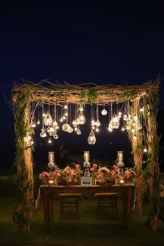 a table with lights and flowers on it under an outdoor gazebo decorated with greenery